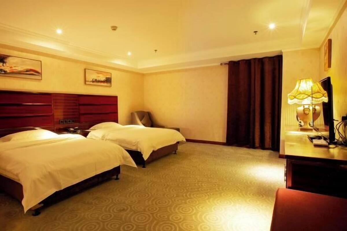 A hotel room with two beds, a desk, a lamp, and a painting on the wall.