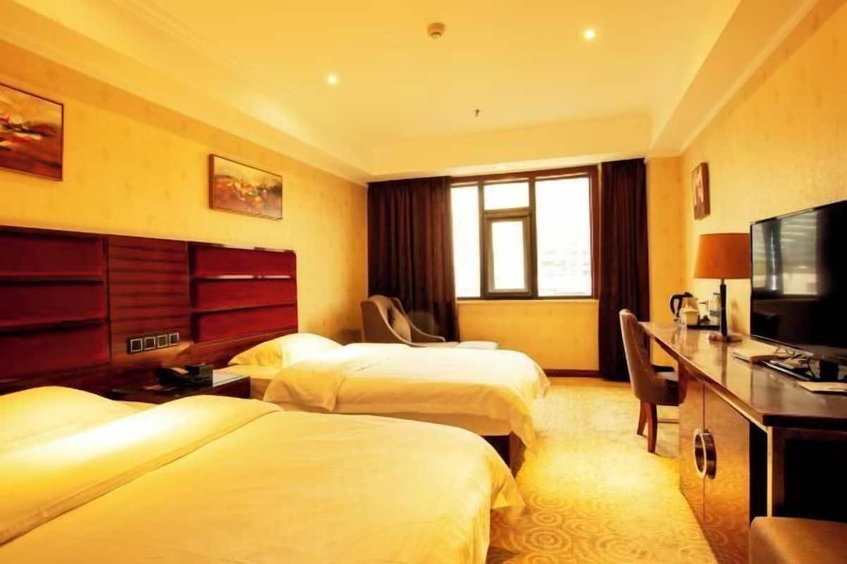 A hotel room with two beds, a desk, a chair, a television, and a window with curtains.