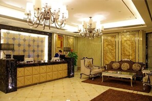 A hotel reception area with a reception desk, a chandelier, a sofa, and a potted plant. - Sunshine Business Hotel (Zhengzhou)