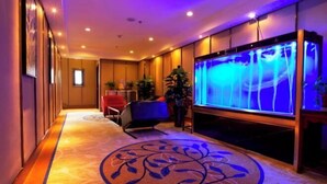 Un pasillo de hotel con un gran acuario, un suelo de diseño y una zona de estar con una silla roja.