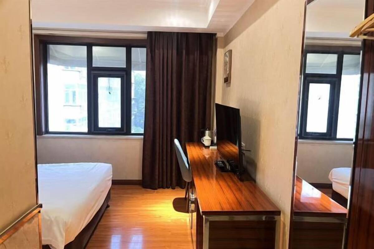 A hotel room with a bed, a desk, a chair, a TV, and a window with curtains.