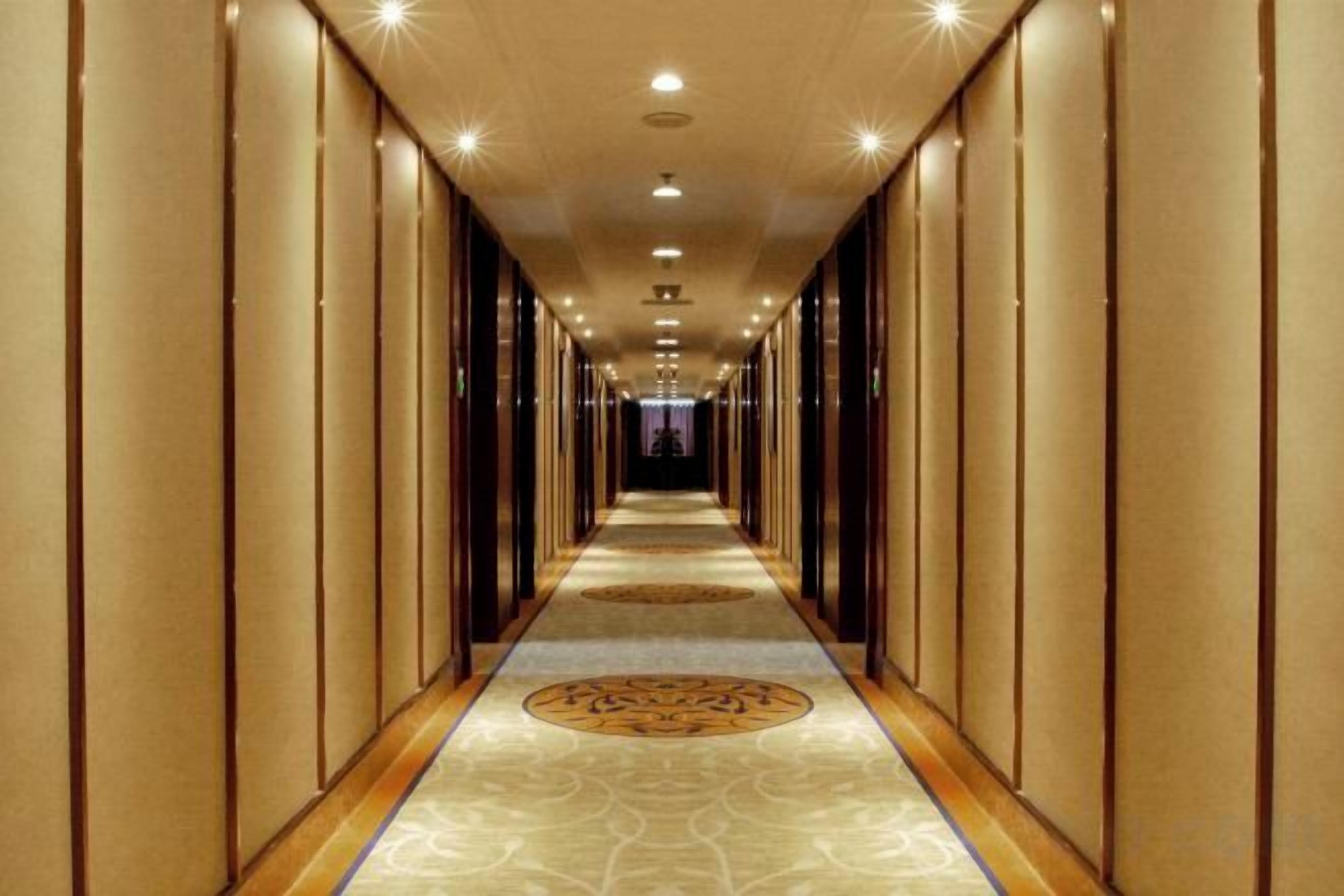 A long, narrow hotel corridor with a patterned carpet and vertical paneling on the walls.