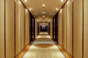 A long, narrow hotel corridor with a patterned carpet and vertical paneling on the walls. - Sunshine Business Hotel (Zhengzhou)