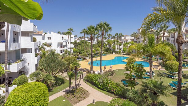 A resort with a central pool, palm trees, and white buildings.