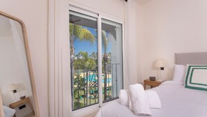 A hotel room with a bed, a nightstand with a lamp, a mirror, and a sliding glass door leading to a pool area.