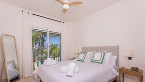 A hotel room with a bed, a nightstand, a mirror, and a view of palm trees and a pool.