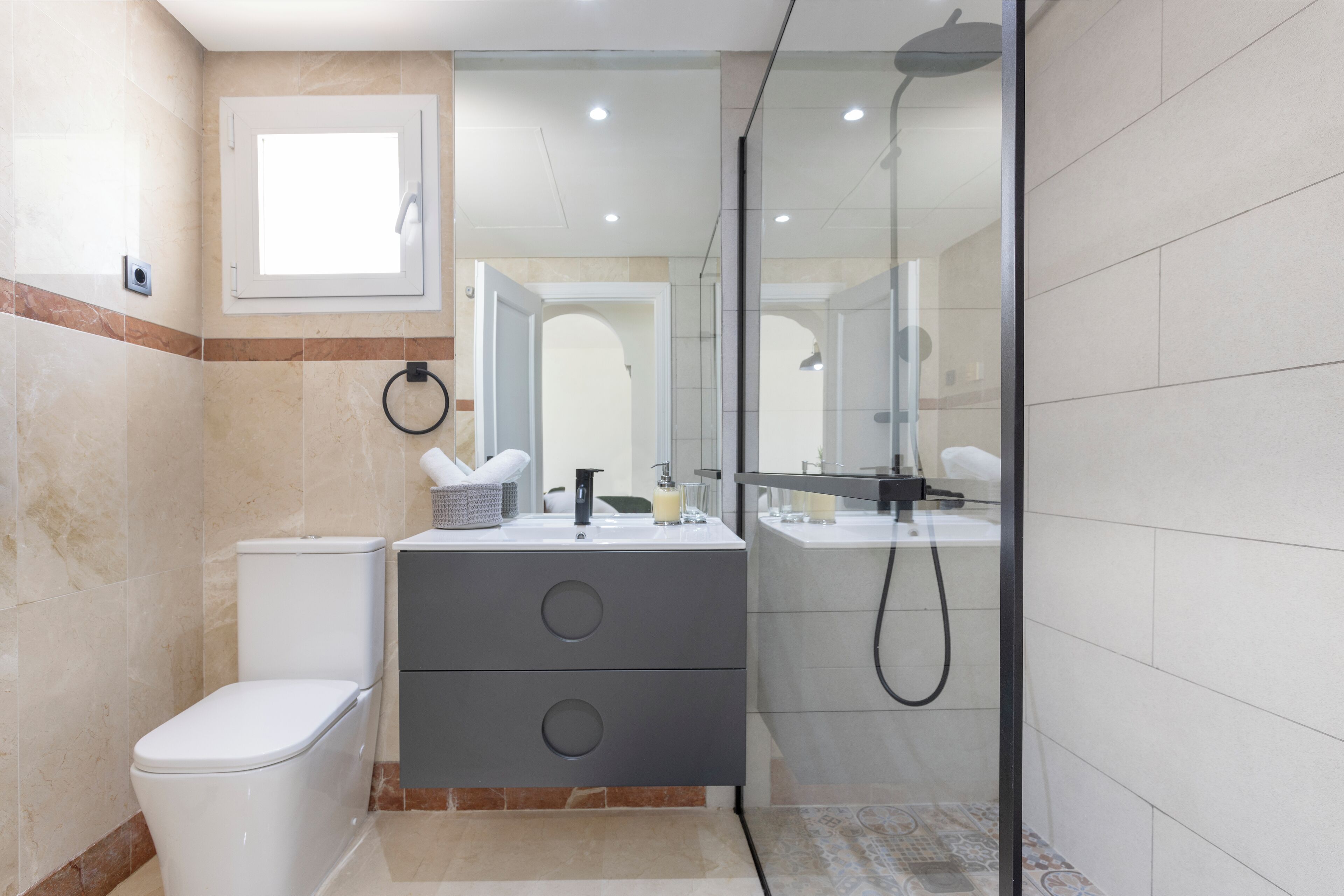 Un baño con inodoro, tocador con espejo y zona de ducha.