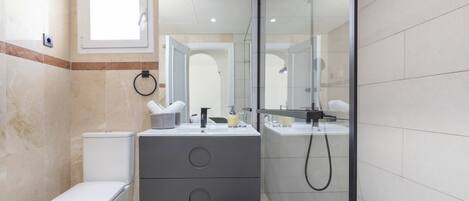 Un baño con inodoro, tocador con espejo y zona de ducha.