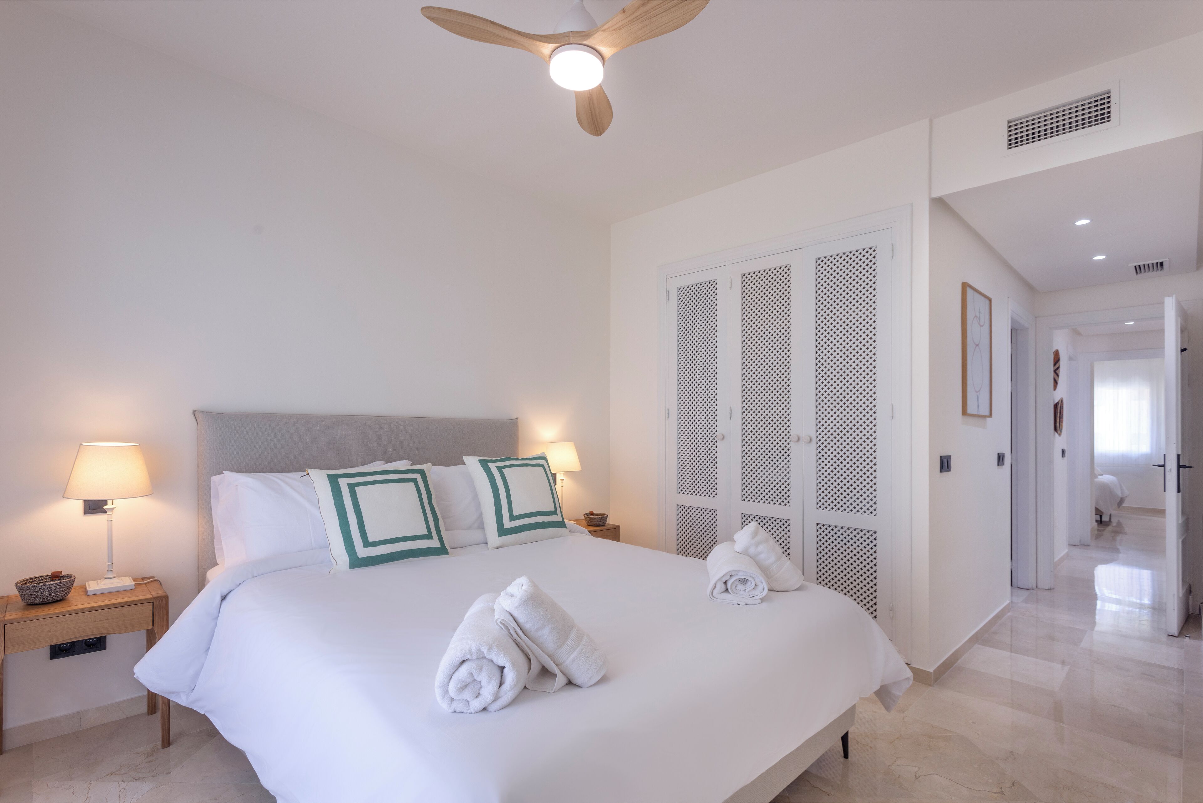 Quarto de hotel com cama grande, duas luminárias de cabeceira, ventilador de teto e closet espaçoso.