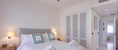 Quarto de hotel com cama grande, duas luminárias de cabeceira, ventilador de teto e closet espaçoso.
