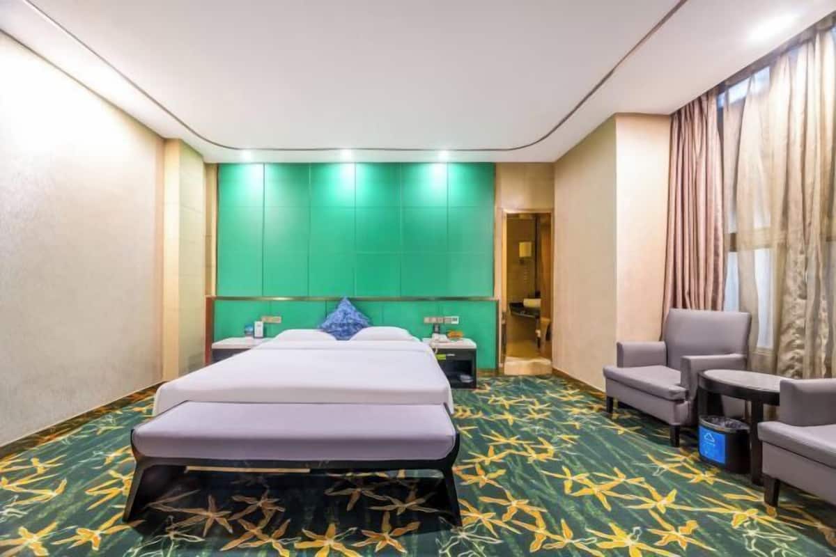 Camera d'albergo con un letto, angolo salotto e parete verde decorativa.