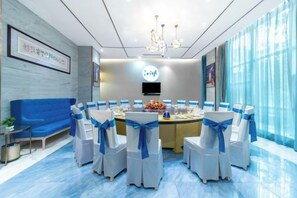 A conference room with a round table, white chairs with blue sashes, a blue sofa, and a chandelier. - Jinhuafu Hotel (Longchang)