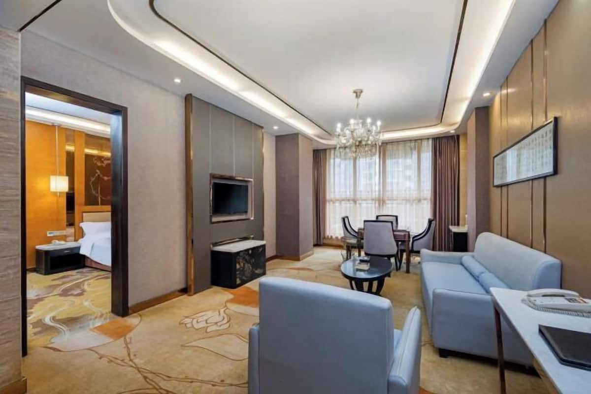 Una moderna camera d'albergo con divano, tavolo da pranzo, televisore e lampadario.