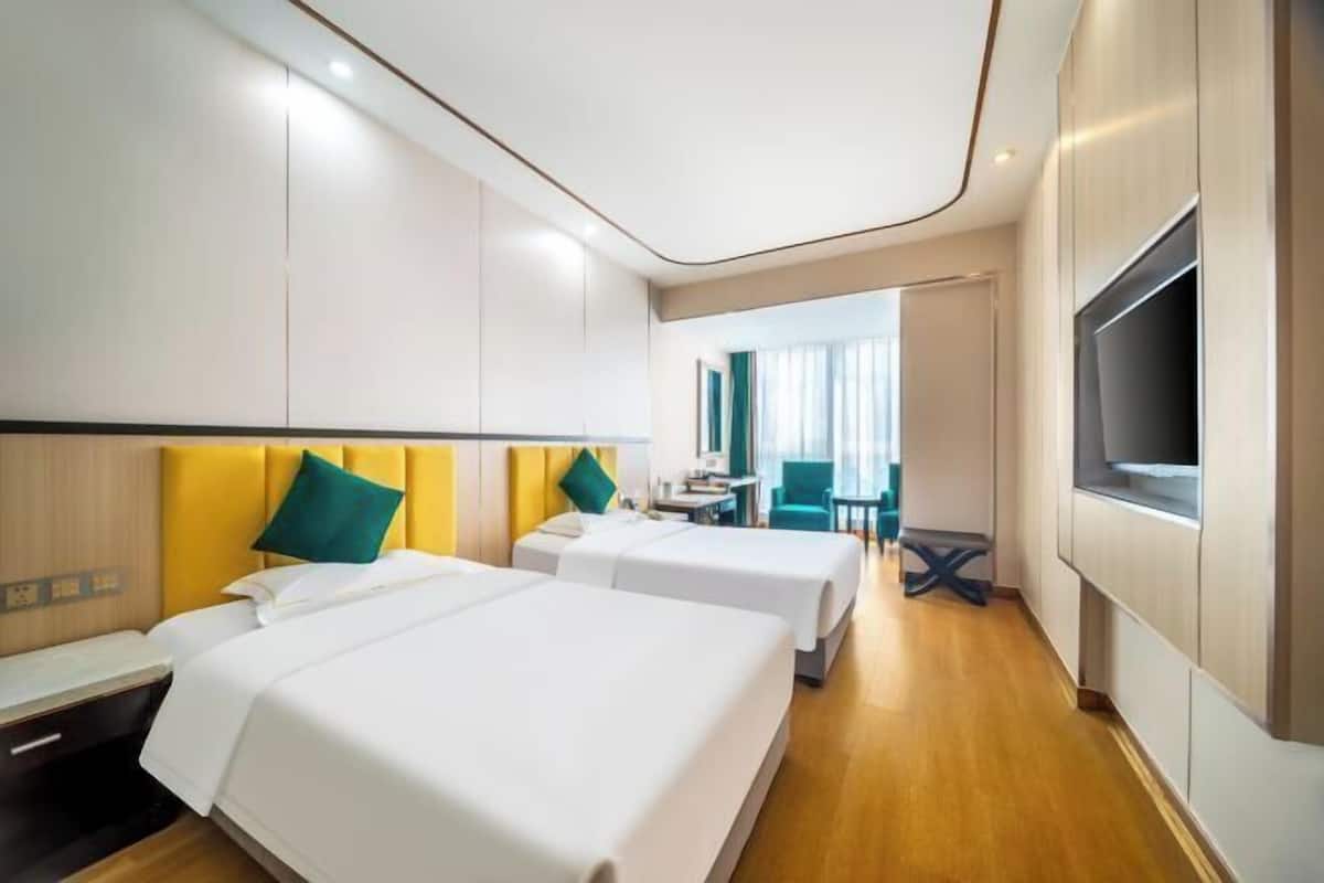 Una camera d'albergo con due letti, una scrivania, una sedia, una televisione e una finestra.