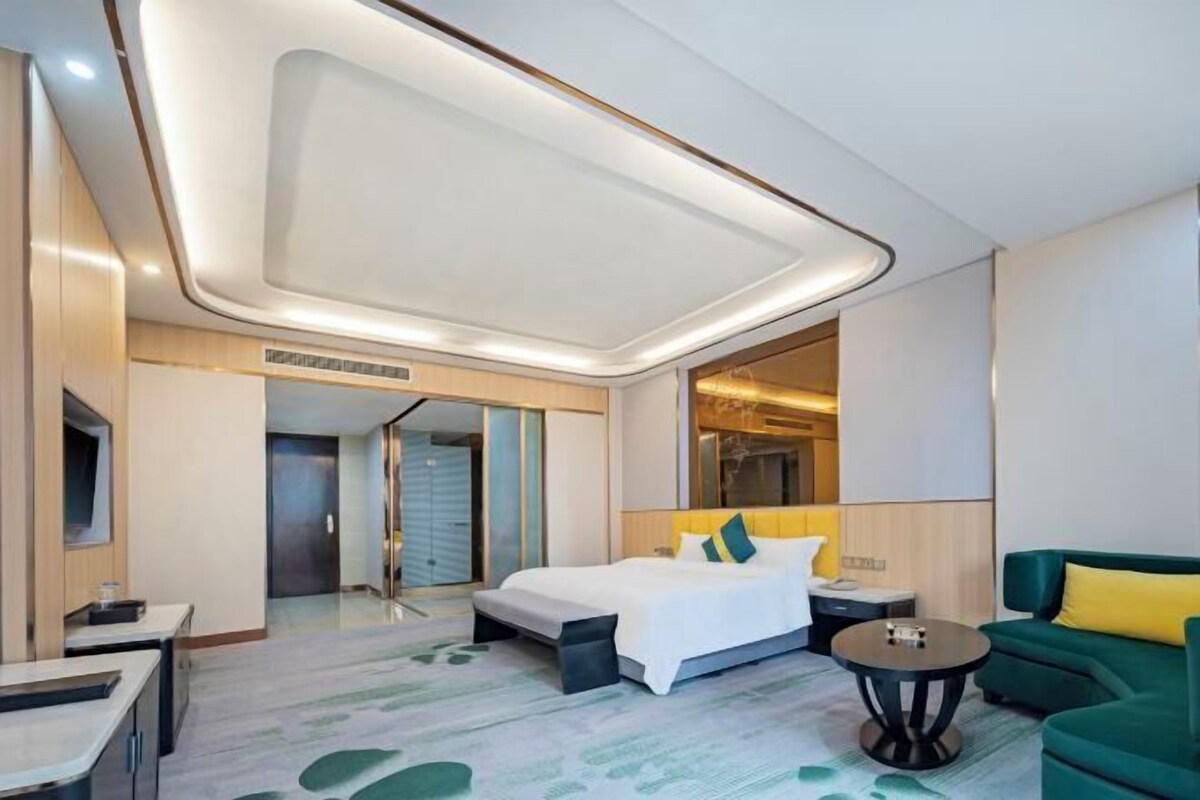 A modern hotel room with a large bed, a green sofa, a small table, and a mirror.