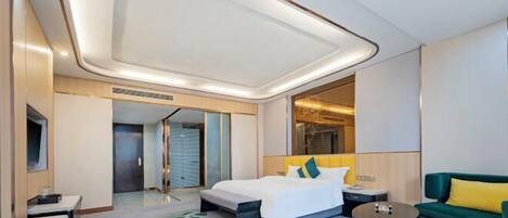 A modern hotel room with a large bed, a green sofa, a small table, and a mirror.