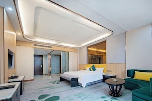 Una habitación de hotel moderna con una cama grande, un sofá verde, una mesita pequeña y un espejo.