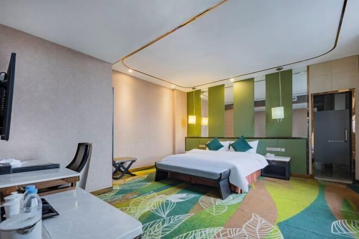A modern hotel room with a bed, bedside table, chair, and a desk with a computer.