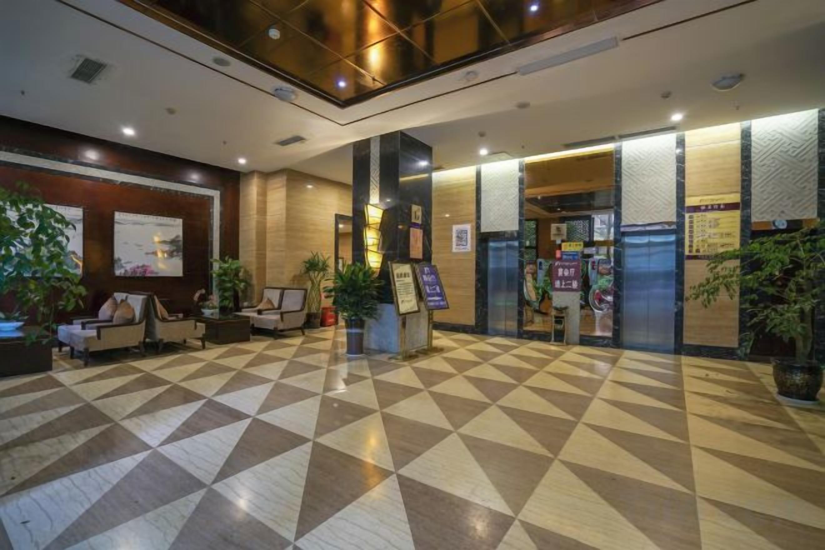 A hotel lobby with a checkered floor, seating area, reception desk, and potted plants.