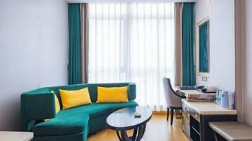 Una habitación de hotel moderna con un sofá verde, una mesa redonda, un escritorio y un gran ventanal con cortinas.