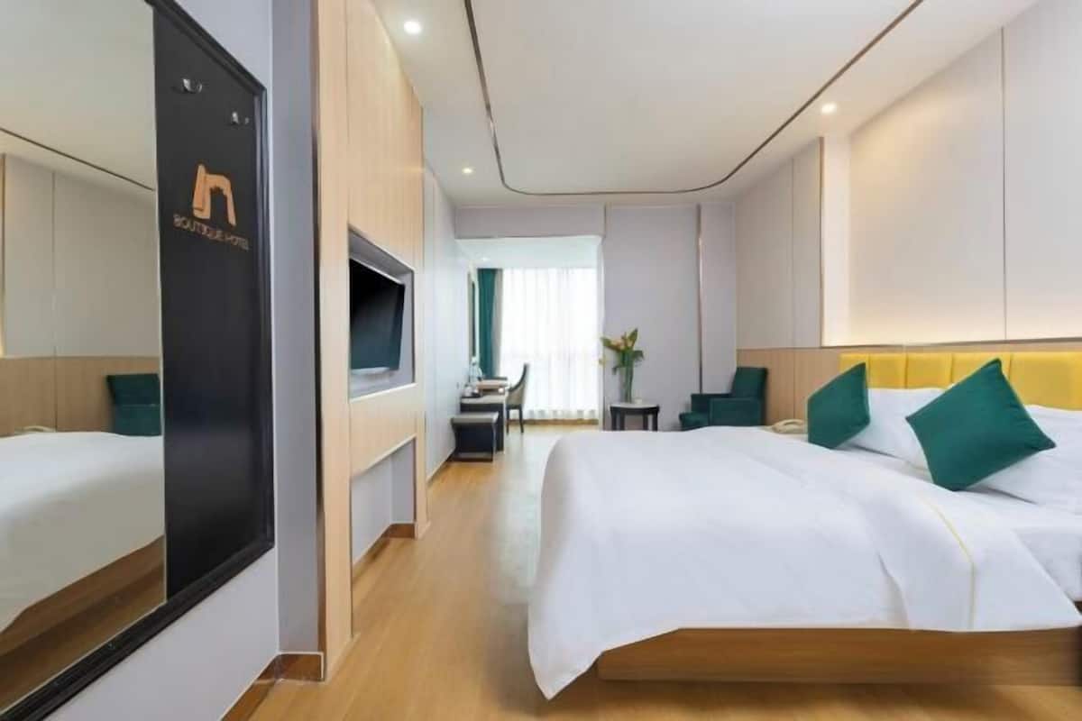 Una camera d'albergo con un letto, una scrivania e una sedia. Si vede una finestra con tende e una pianta nella stanza.
