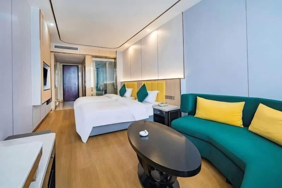 Una camera d'albergo moderna con un letto, una poltrona verde, un tavolino e una scrivania.
