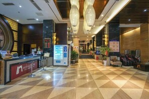 Een hotelhal met een receptiebalie, automaten en zithoeken.