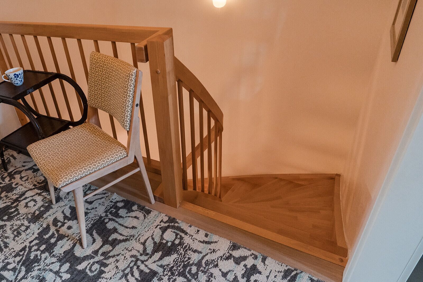 Una silla de madera con un cojín estampado, una mesita con una taza, y una escalera de madera.