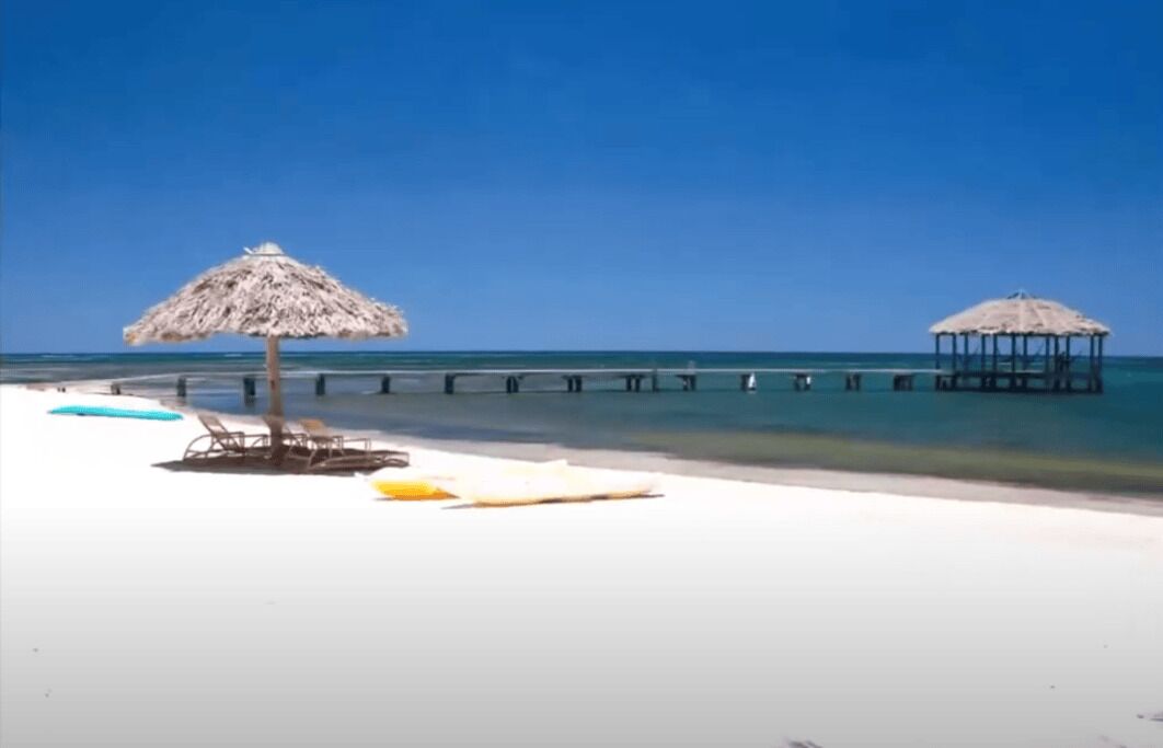 Une plage avec des parasols en chaume, des chaises longues et une jetée qui s’avance dans l’eau.