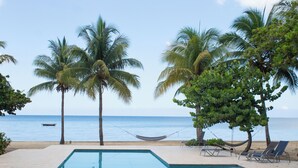 A pool area with a hammock, lounge chairs, and palm trees overlooking the ocean.