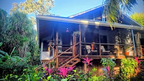 Una casa moderna con porche cubierto, escaleras de madera y exuberante vegetación tropical.