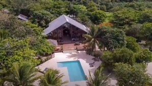An aerial view of a resort with a pool, surrounded by lush greenery and palm trees.