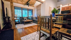 A cozy living room with a wooden ceiling, a sofa, a coffee table, and a dining area with a wooden chair and table.