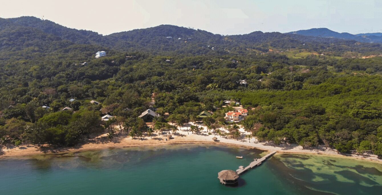 An aerial view of a coastal area with a beach, houses, and a dock.