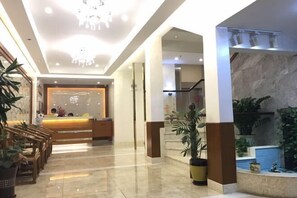 Een hotel lobby met een receptiebalie, een zithoek en potplanten.