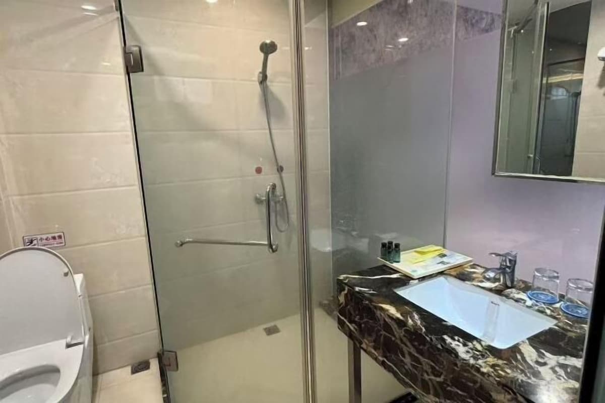 Une salle de bain dotée d’une douche à parois de verre, d’un comptoir en marbre et d’un lavabo avec un miroir au-dessus.