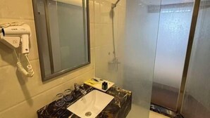 Een badkamer met een marmeren wastafel, een haardroger en een douche met glazen wanden.