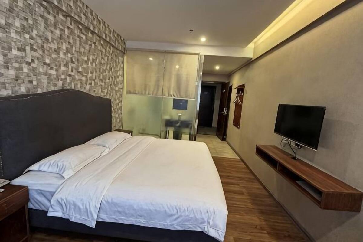 Une chambre d’hôtel avec un lit, un téléviseur, un banc en bois et un mur décoré de motifs.