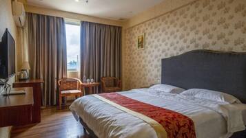 A hotel room with a bed, a desk, a chair, and a window with curtains.
