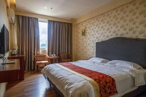 Een hotelkamer met een bed, een bureau, een stoel en een raam met gordijnen.