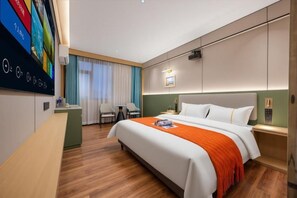 Een hotelkamer met een groot bed, een bureau, een stoel en een televisie aan de muur.