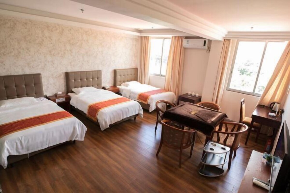 Une chambre d’hôtel avec deux lits, une table à manger, des chaises, un petit tabouret, une télévision et un appareil de climatisation.