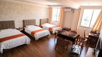 A hotel room with two beds, a dining table, chairs, a small stool, a TV, and an air conditioning unit.