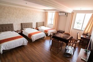 Een hotelkamer met twee bedden, een eettafel, stoelen, een klein krukje, een televisie en een airconditioner.