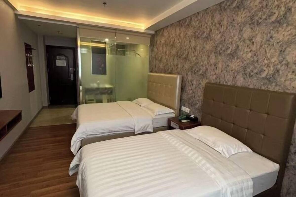 Une chambre d’hôtel avec deux lits, un plancher en bois, un mur en marbre et une cabine de douche en verre.