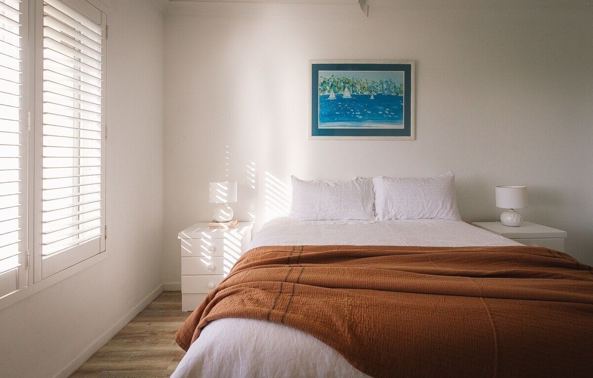A bedroom with a bed, white nightstands, a lamp, and a painting on the wall.