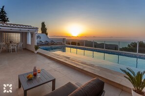 Una piscina al terrat amb vistes al capvespre, mobiliari exterior i zona de dinar.