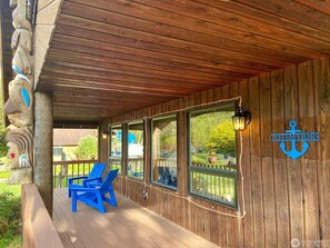 A wooden deck with blue chairs and a table, a wooden wall with windows, and a sign reading "TOTEM TIDES".