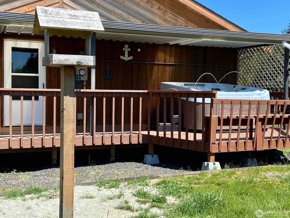 A wooden cabin with a covered deck, an anchor decoration, and a hot tub.