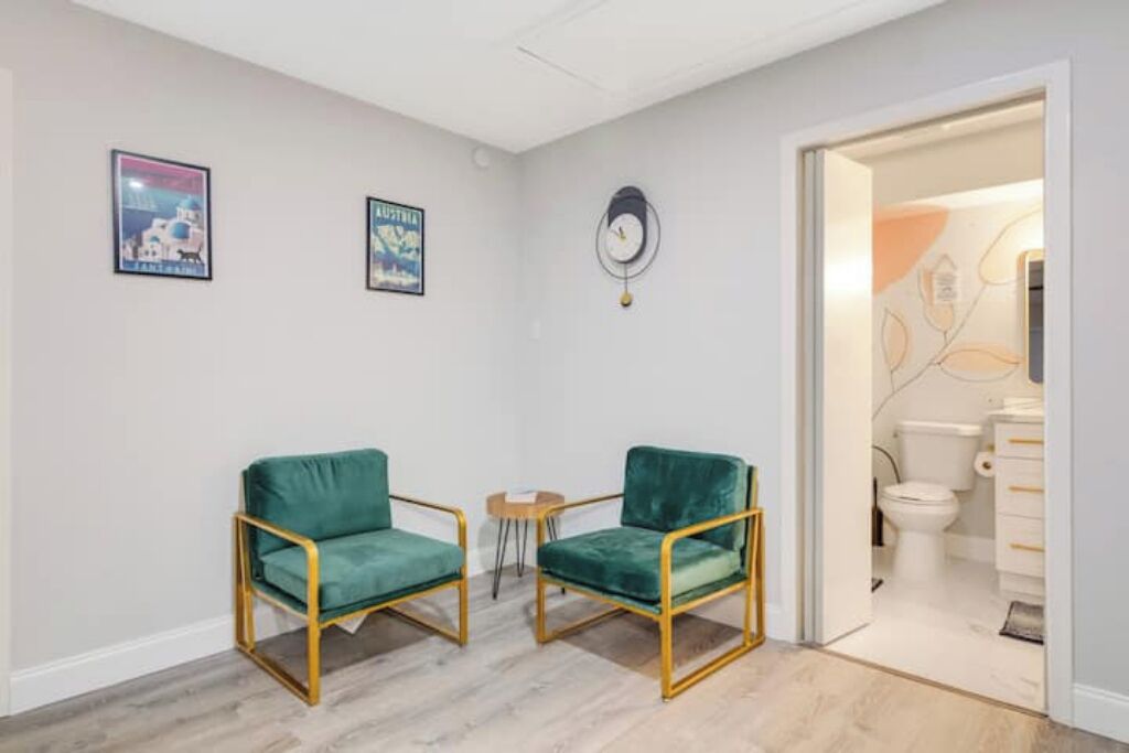 Une pièce comprenant deux fauteuils en velours vert à cadre doré, une petite table en bois et une horloge murale.